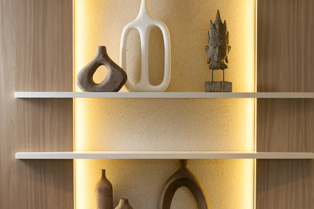 Nicho iluminado no consultório, com vasos de cerâmica e uma escultura em prateleiras claras.