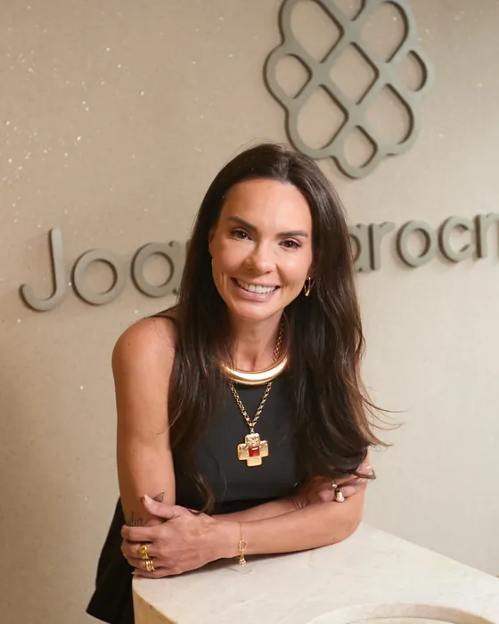 Dra. Joana Iarocrinski na recepção do consultório, com a marca na parede ao fundo.