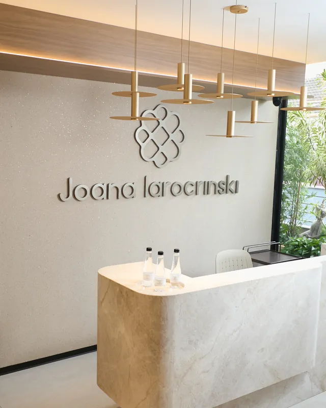 Recepção do consultório da Dra. Joana Iarocrinski no Bigorrilho, em Curitiba, com balcão de mármore, luminárias douradas e a marca na parede.